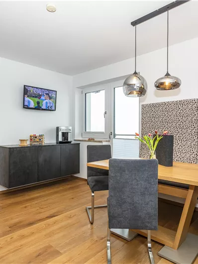 Een moderne woning met een houten tafel en elegante stoelen. Grote ramen zorgen voor veel licht en een gezellige woonruimte.