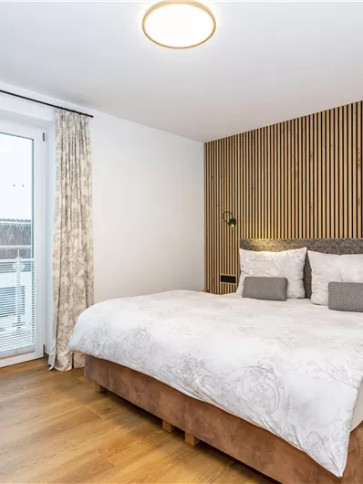 Een moderne slaapkamer met een groot bed en houten wandbekleding. De ruimte heeft een heldere sfeer en toegang tot een balkon.