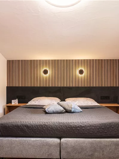 Een moderne slaapkamer met een groot bed en elegante verlichting. De muren zijn eenvoudig en de vloer is van hout, wat een gezellige sfeer creëert.
