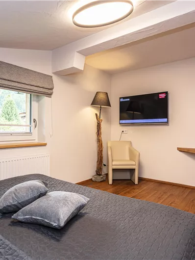 Een gezellige slaapkamer met een groot bed, twee kussens en een televisie aan de muur. De kamer heeft een moderne houten kast en aangenaam licht.