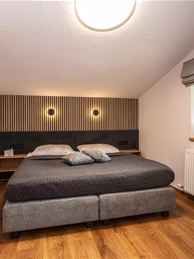 Een moderne slaapkamer met een groot bed en mooie houten bekleding. Grote ramen zorgen voor veel daglicht en een prettige sfeer.