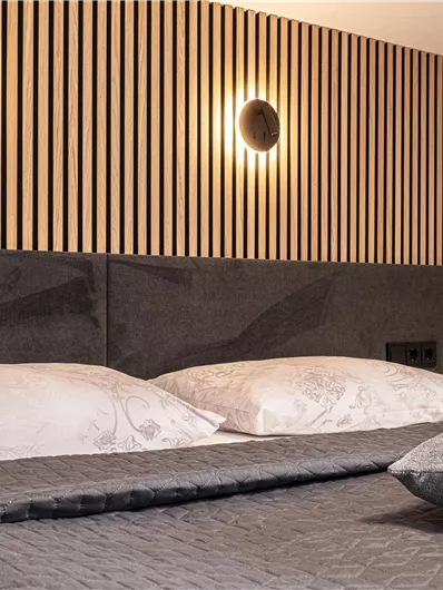 Een moderne slaapkamer met een elegant bed en zachte verlichting. De muren zijn versierd met houten latten, wat een gezellige sfeer creëert.