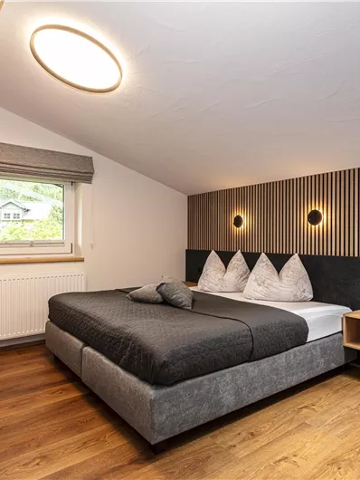 Een moderne slaapkamer met een tweepersoonsbed en een gezellige zithoek. De wanden zijn in houtlook ingericht en het licht zorgt voor een aangename sfeer.