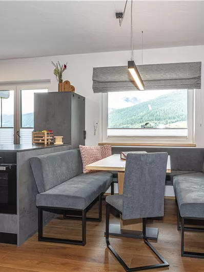 Een moderne keuken met een eetgedeelte van grijze meubels. Op de achtergrond zijn ramen met uitzicht op de bergen en een interessante wanddecoratie te zien.