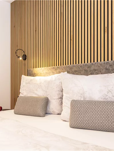 Een moderne slaapkamer met een verhoogde houten hoofdeinde en gezellige kussens. De zachte verlichting zorgt voor een ontspannende sfeer.