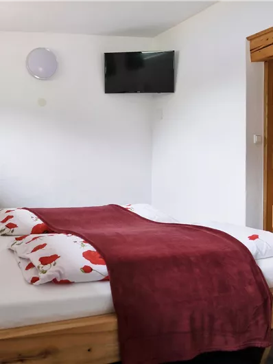 A cozy bedroom with a large bed and blooming cushions. There is a television on the wall and a nice wooden table in the room.