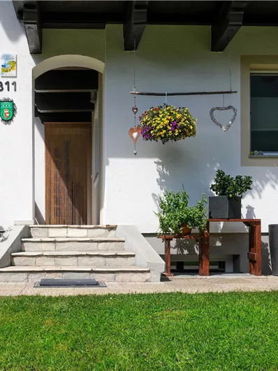 A well-maintained entrance area with a stone staircase and colorful flowers. The house has large windows and a beautiful view of the surrounding nature.