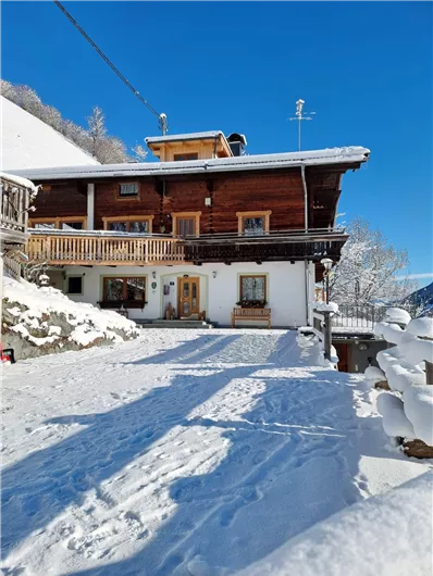 A charming wooden house in the snow with a clear blue sky. The area is surrounded by a beautiful winter landscape.