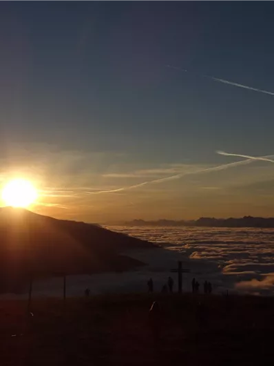 Ein spektakulärer Sonnenuntergang über den Bergen, mit Wolken, die das Tal füllen. Die goldenen Strahlen der Sonne erhellen die Landschaft.