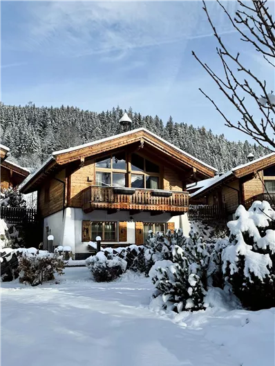 Ein gemütliches Holzhaus im Schnee, umgeben von schneebedeckten Bäumen. Die Landschaft ist winterlich und friedlich.