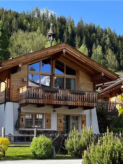 Ein wunderschönes Holzhaus inmitten von Bäumen und grüner Landschaft. Der Himmel ist klar und blau.