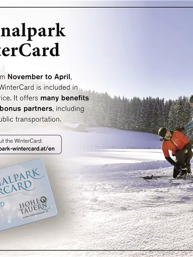 Ein Werbebild für die Nationalpark WinterCard zeigt zwei Personen beim Skifahren in einer verschneiten Landschaft. Die Karte bietet Vorteile und wird von November bis April beim Unterkunftsbooking eingeschlossen.