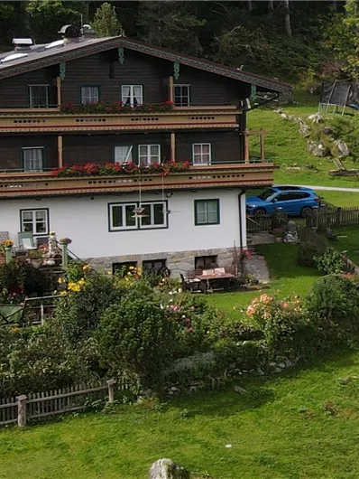 Ein gemütliches Haus in ländlicher Umgebung, umgeben von Grünflächen und Bäumen. Der Garten ist gepflegt und es sind einige Steine sichtbar.