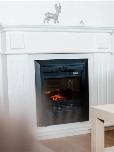 Ein moderner Kamin in einem hellen Raum mit hellem Holzfußboden. Der Kamin hat eine schlichte schwarze Front und eine elegante weiße Umrandung.