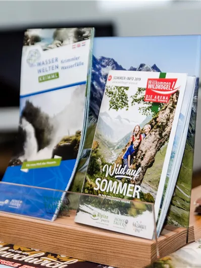 Ein Ständer mit Prospekten zu Urlaubsangeboten in den Bergen. Die Broschüren zeigen Natur- und Freizeitaktivitäten für den Sommer.