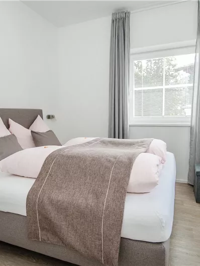 Ein gemütliches Schlafzimmer mit einem großen Bett und weichen Kissen. Die hellen Wände und Vorhänge sorgen für eine freundliche Atmosphäre.