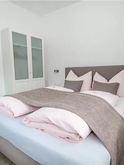 Een moderne slaapkamer met een groot bed en ruime, lichte inrichting. Het beddengoed is licht en gezellig, ideaal om te ontspannen.