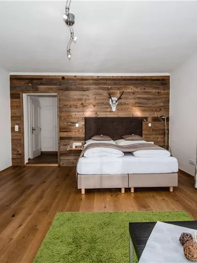 Een gezellige kamer met een tweepersoonsbed en houten muren. De inrichting omvat een kleine kitchenette en een zithoek met een groene vloerkleed.