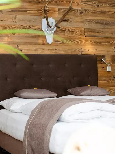 Een gezellige slaapkamer met een modern bed en een houten wandbekleding. Op de achtergrond zijn een hertengewei en een groene plant te zien.