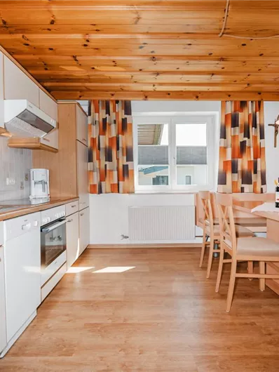 A modern kitchen with a wooden ceiling and a dining table.
Bright colors and windows create a friendly atmosphere.