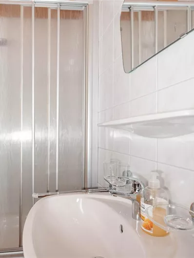A modern bathroom with a shower and a sink. The walls are tiled with light tiles and there are some toiletries on the sink.