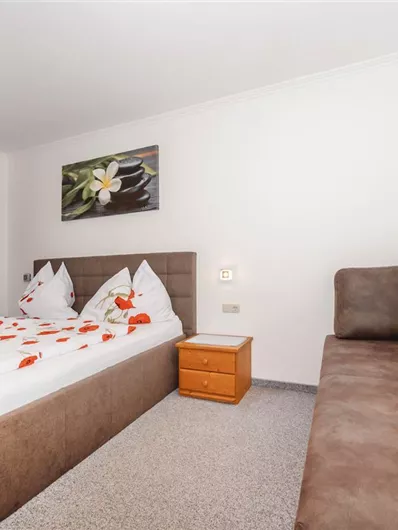 A bright room with a double bed and a cozy couch. Red curtains and a wall painting create a pleasant atmosphere.