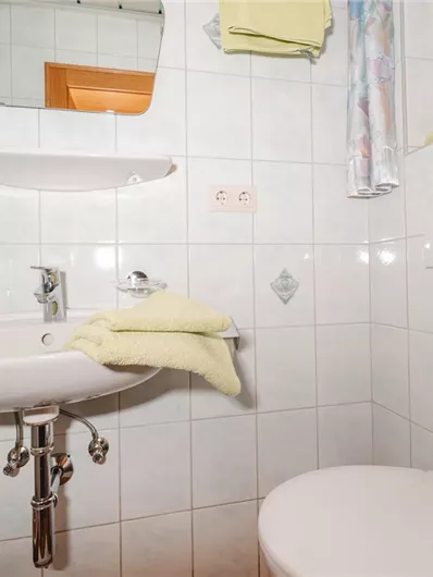 A small, modern bathroom with a sink and toilet. There are bright tiles and a yellow towel visible.