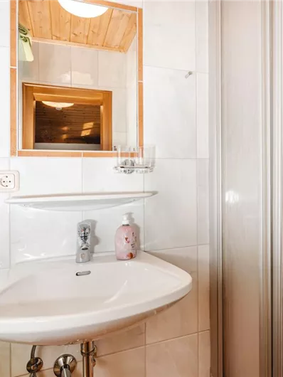 A modern bathroom view with a sink, a mirror, and a shower. A hairdryer hangs on the wall and a green towel is on the shelf.