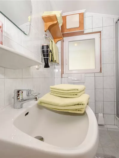 A modern bathroom with a bright tiled floor. On the sink are yellow towels and there is a shower in the background.
