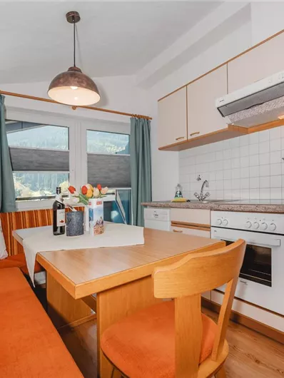 A modern kitchen with a dining table and a cozy bench. Large windows provide plenty of light.