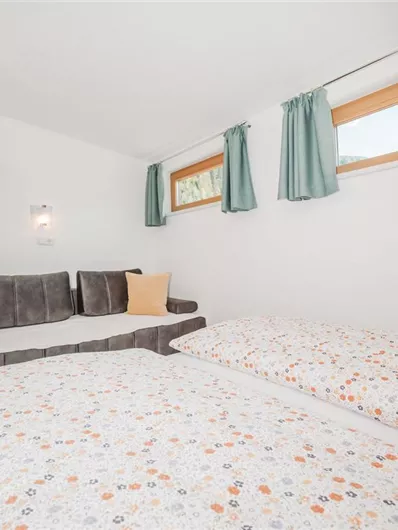 A cozy room with two beds and a sofa bed. The bright walls and windows create a friendly atmosphere.
