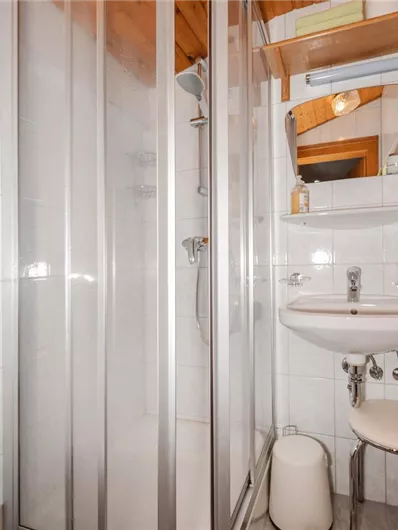 A modern bathroom with a shower and sink. It is bright and clean, with white tiles and wood paneling.