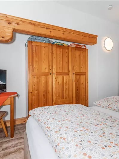 A cozy room with two single beds and wooden-colored furniture. There is a table with a chair and a television on the wall.