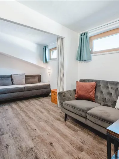 A bright room with two sofas and wooden flooring. Large windows provide plenty of natural light.