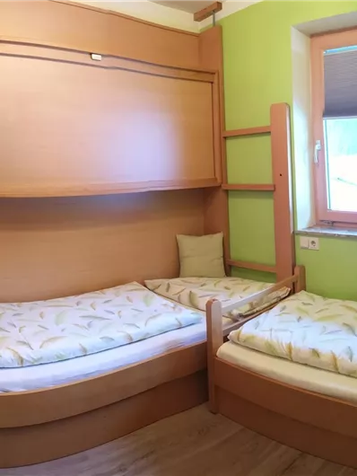 A simple room with two beds and a sink. The walls are painted green and there is a window with a view outside.