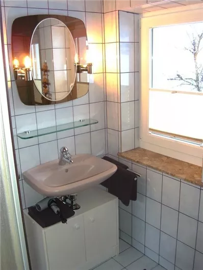 A modern bathroom with a sink, a mirror, and a window. The walls are tiled and there are towels in dark colors.