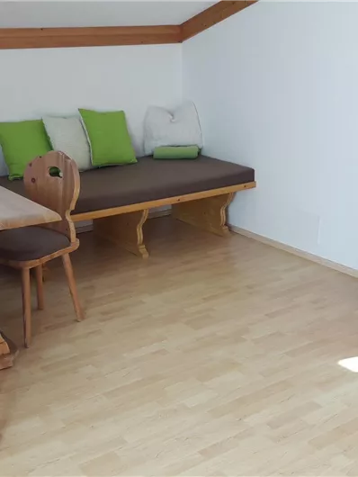 Een gezellige woonkamer met een tafel, houten stoelen en een bank. In de ruimte staat een televisie op een houten kast.
