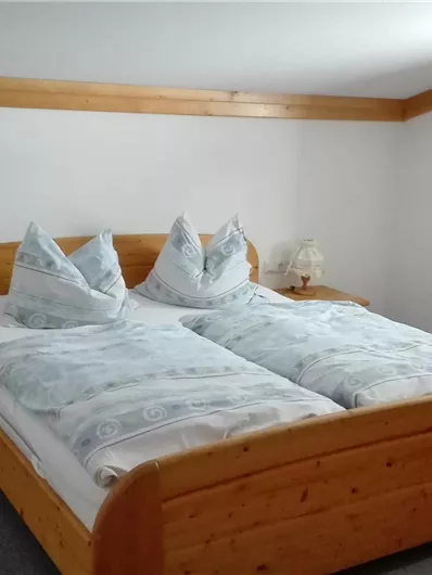 Een gezellige slaapkamer met een houten bed en twee kussens. De ruimte is helder en vriendelijk ingericht, met een kleine nachtlamp en een raam.