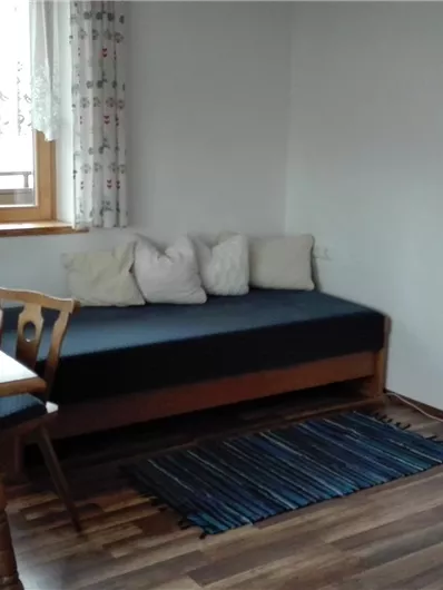 Een gezellige woonkamer met een bank, een eettafel en een televisie. Grote ramen laten veel licht binnen.