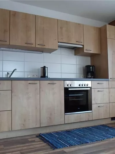 Een moderne keuken met houten kasten en een fornuis. De vloer is bedekt met een blauwe loper.