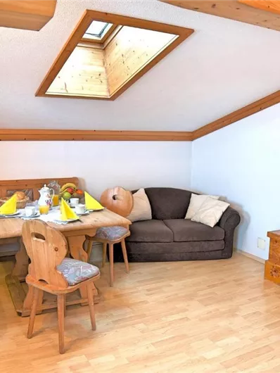 Een gezellige woonkeuken met houten meubels en een eettafel. Een bank en een televisie completeren de ruimte onder een dakraam.