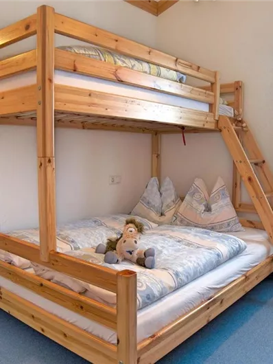 Een gezellige kinderkamer met een stapelbed van hout. Daaronder staat een groot bed, en een knuffel ligt op de deken.