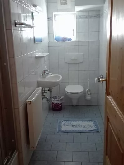 Een moderne badkamer met lichte tegels en een groot raam. Er is een wastafel, een toilet en een douche.