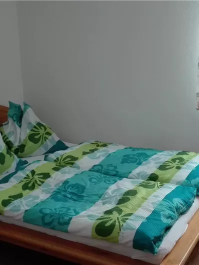 Een gezellige slaapkamer met een tweepersoonsbed en kleurrijke beddengoed. Een raam laat natuurlijk licht binnen, en er is een verwarming aan de muur.