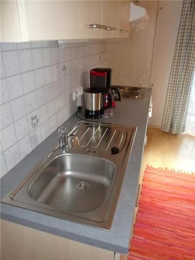 Een moderne keuken met een gootsteen en een waterkoker. Naast de gootsteen ligt een klein, kleurrijk vloerkleed op de vloer.