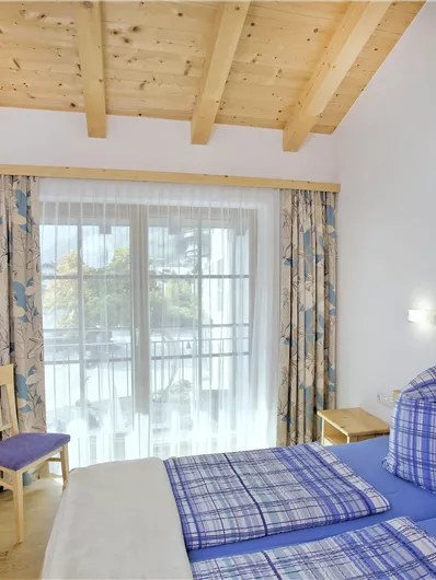 Een gezellige slaapkamer met twee bedden en een houten plafond. Er is een tv en grote ramen met mooi licht.