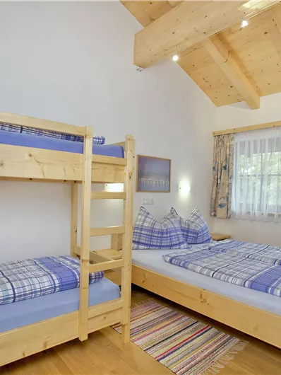 Een gezellige slaapkamer met een stapelbed en een tweepersoonsbed. Grote ramen zorgen voor veel daglicht en een aangename sfeer.