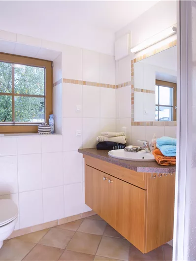 Een moderne badkamer met tegels en houten kasten. Er is een raam, een douche en frisse handdoeken.