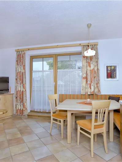 Een gezellige keuken met eetruimte en televisie. Er zijn lichte meubels en grote ramen die veel licht binnenlaten.