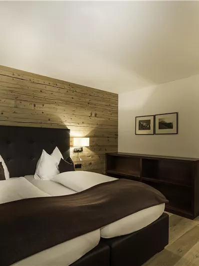 A modern hotel room with a large double bed and wooden paneling. The decor is elegant and cozy, perfect for a relaxing stay.